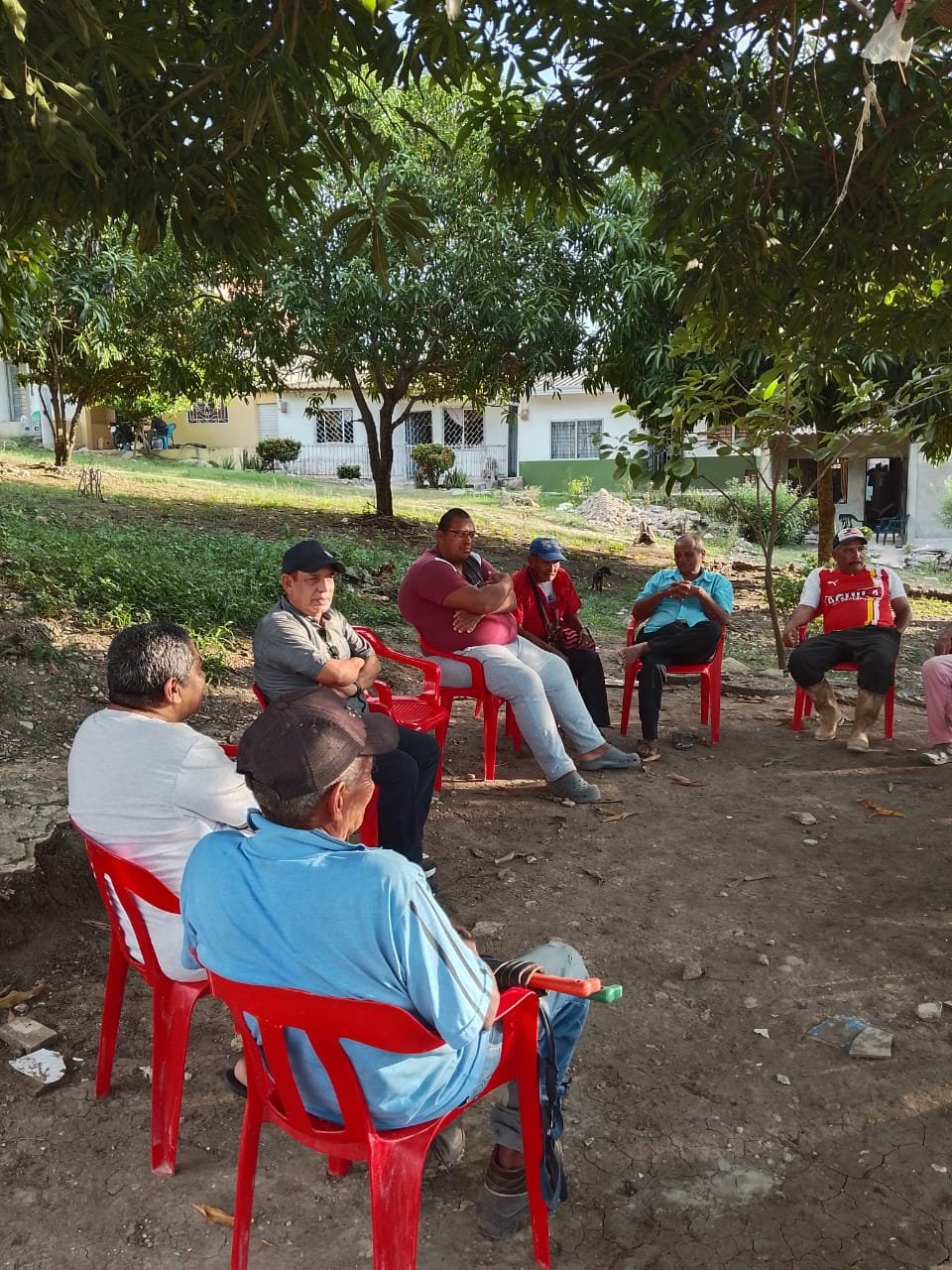 Everardo en reunión con vecinos bajo los árboles